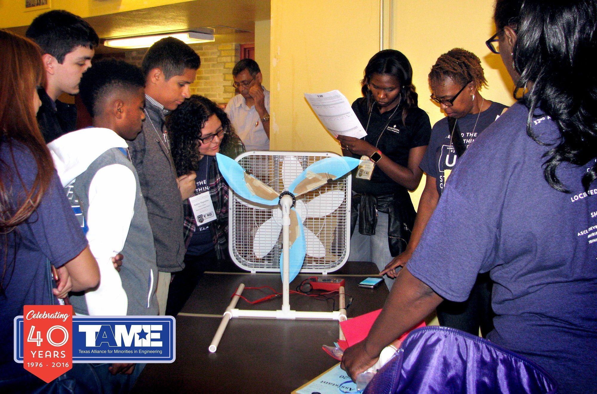 Six diverse students hold up a prototype of a Wind Turbine made from cardstock and craft supplies. From the Engineering Design Challenge at the 2017 State STEM Competition in San Antonio, TX.