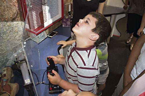 6 yr old Brayden Nall at Robotic Arm Exhibit of TAME's Trailblazer Mobile Science Museum at the Library of Graham, Photo by Brian Rash of GrahamLeader