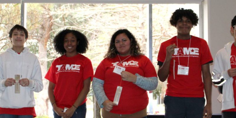 Six students wearing red TAME shirts hold up silver ribbons during the Awards Ceremony at the 2020 Dallas Divisional STEM Competition. The students' ages range from grade 6 to grade 12.