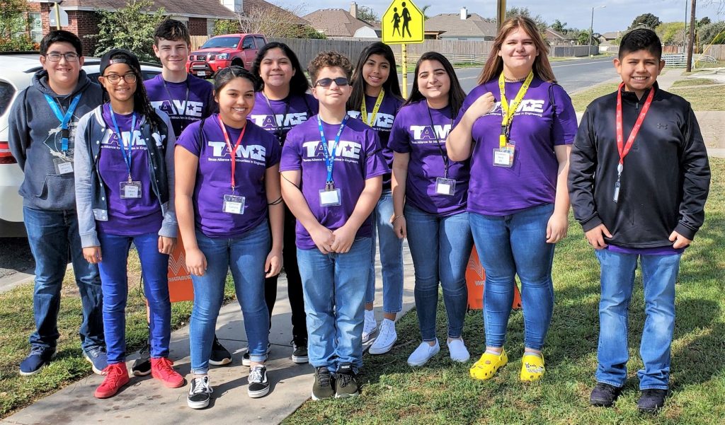 Ten middle school students in purple TAME shirts stand outside near a school.