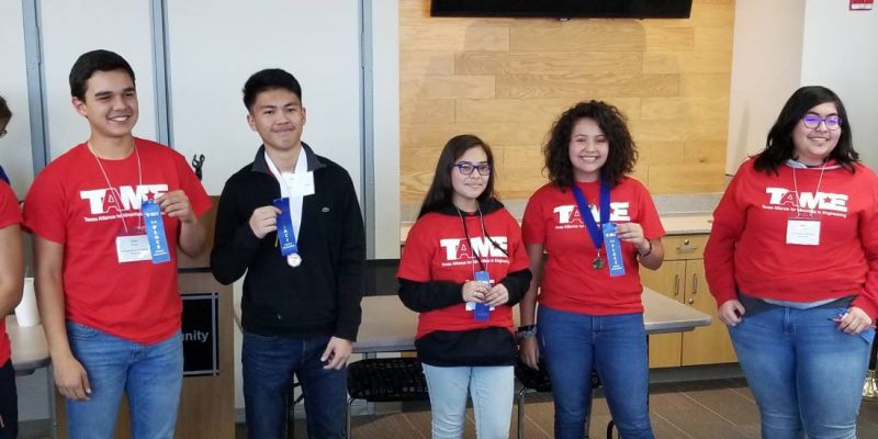 Three male students and three female students wearing red TAME shirts hold up blue ribbons during the Awards Ceremony at the 2020 West Texas Divisional STEM Competition. The students' ages range from grade 6 to grade 12.