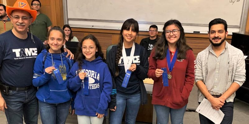 Six students wearing TAME shirts and school shirts from the Valley hold up blue ribbons during the Awards Ceremony at the 2020 Valley Divisional STEM Competition. The students' ages range from grade 6 to grade 12.