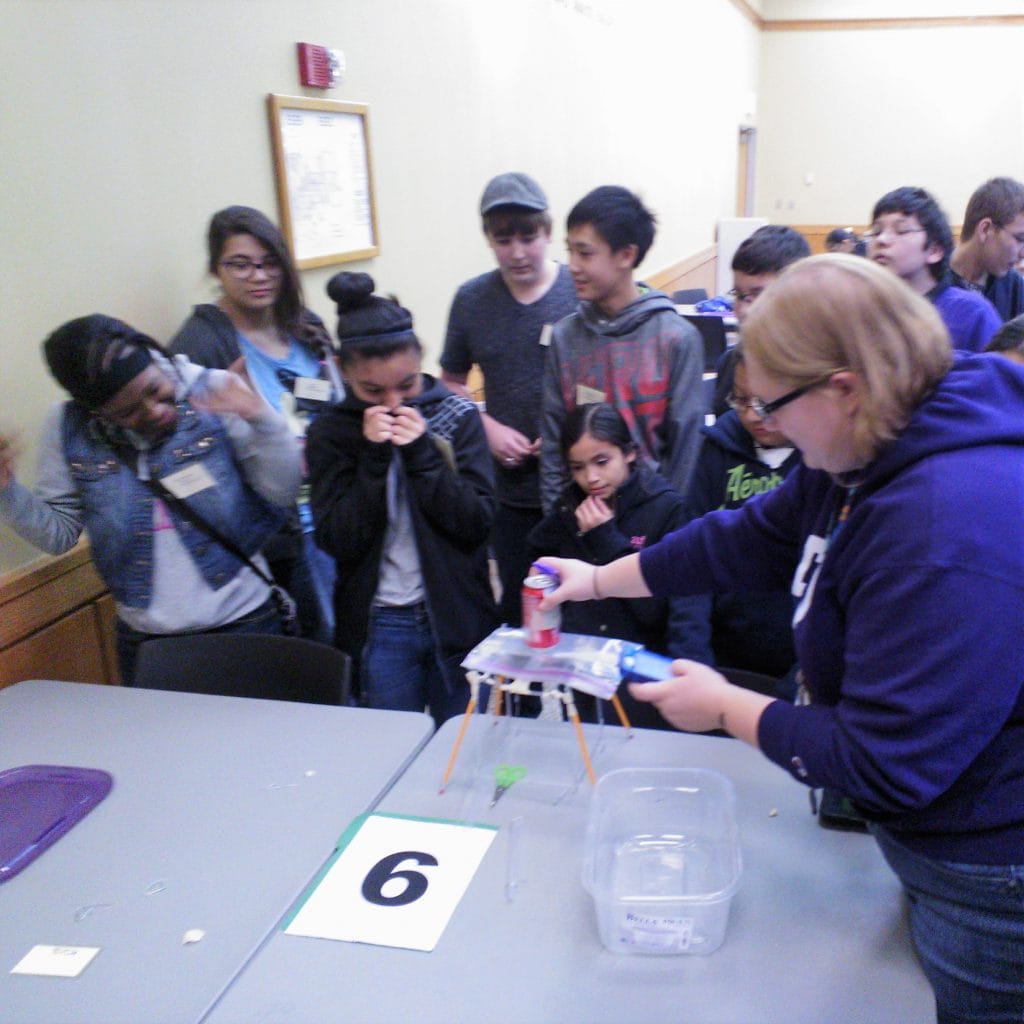 Students react as a volunteer Engineering Design Challenge Judge tests a student prototype at the 2014 Dallas Divisional Math & Science Competition, hosted at Tarrant County College.