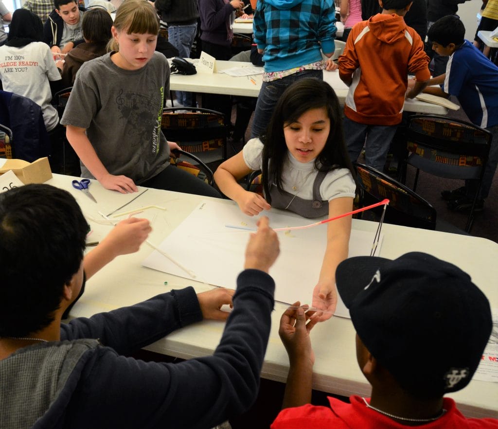 A young woman discusses her engineering prototype with her team. 